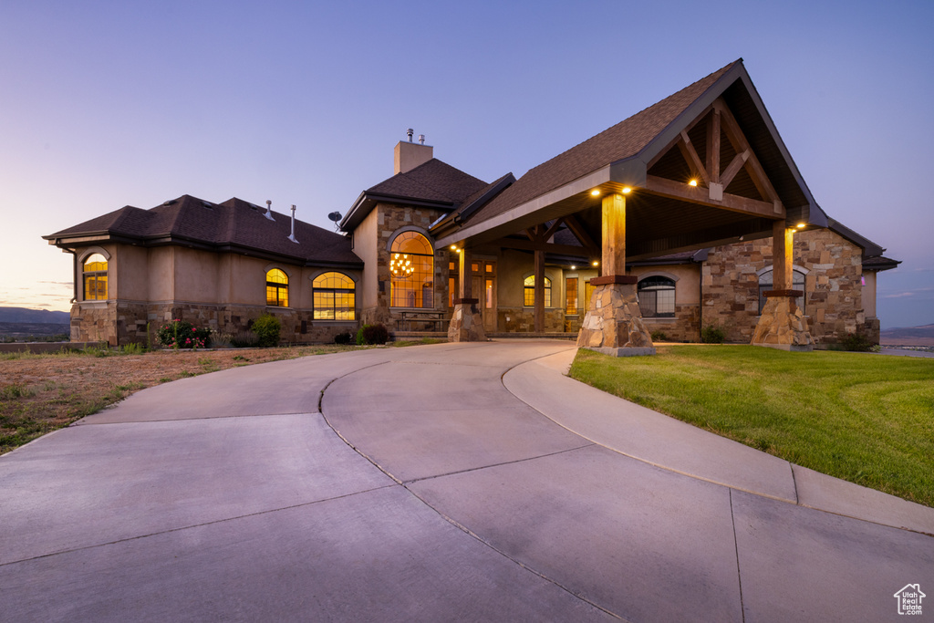 View of front of property featuring stone siding, a chimney, a front lawn, curved driveway, and roof with shingles