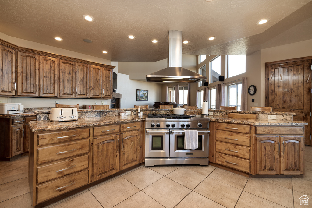 Kitchen with range with two ovens, range hood, recessed lighting, a peninsula, and stone counters