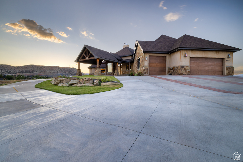 View of front of house featuring a garage, stone siding, driveway, a chimney, and stucco siding