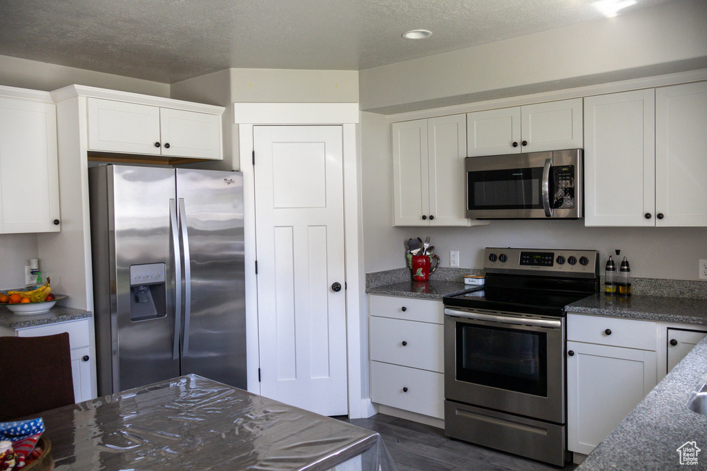 Kitchen featuring stainless steel appliances, white cabinetry, dark wood-style floors, a textured ceiling, and dark stone countertops