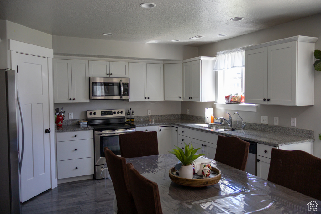 Kitchen featuring appliances with stainless steel finishes, a textured ceiling, white cabinetry, recessed lighting, and dark wood finished floors