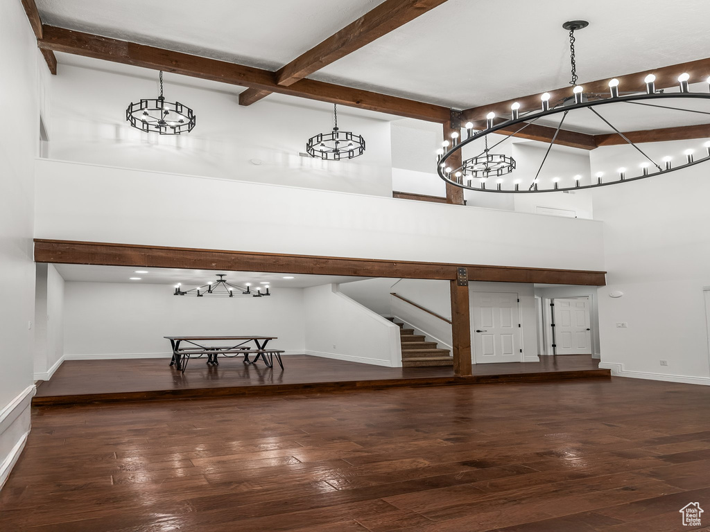 Unfurnished dining area featuring beamed ceiling, a chandelier, a high ceiling, hardwood / wood-style floors, and stairway