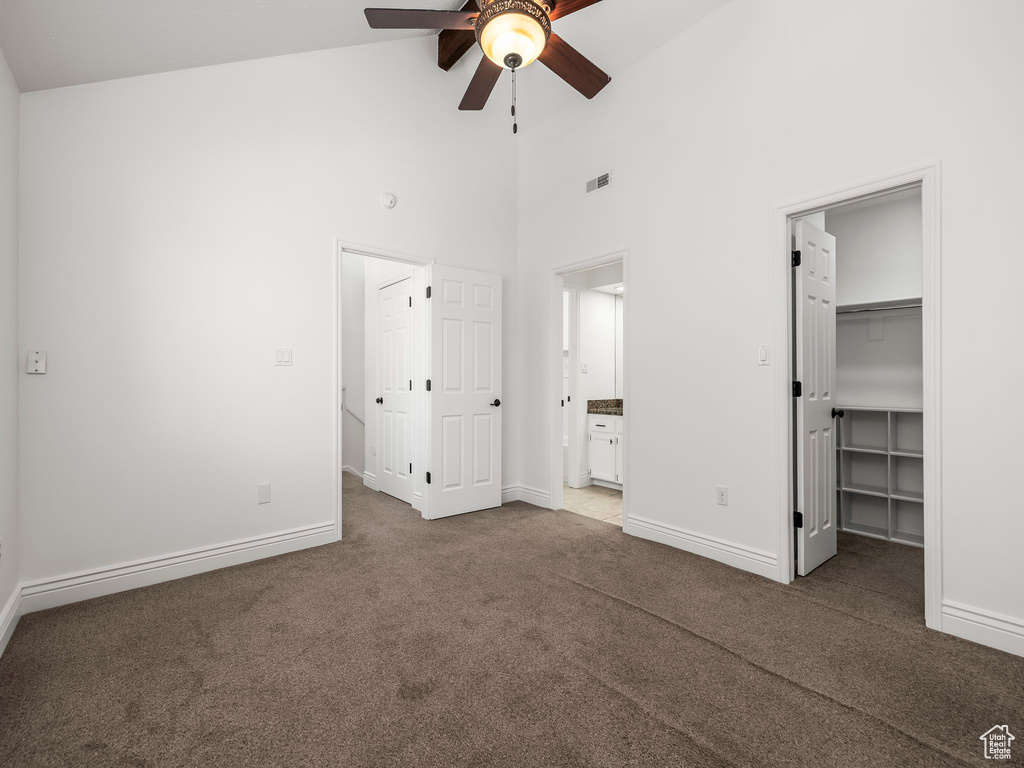 Unfurnished bedroom with high vaulted ceiling, a spacious closet, carpet floors, ensuite bath, and ceiling fan