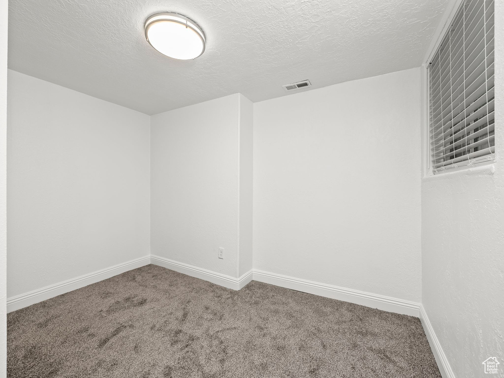 Carpeted empty room featuring a textured ceiling and baseboards