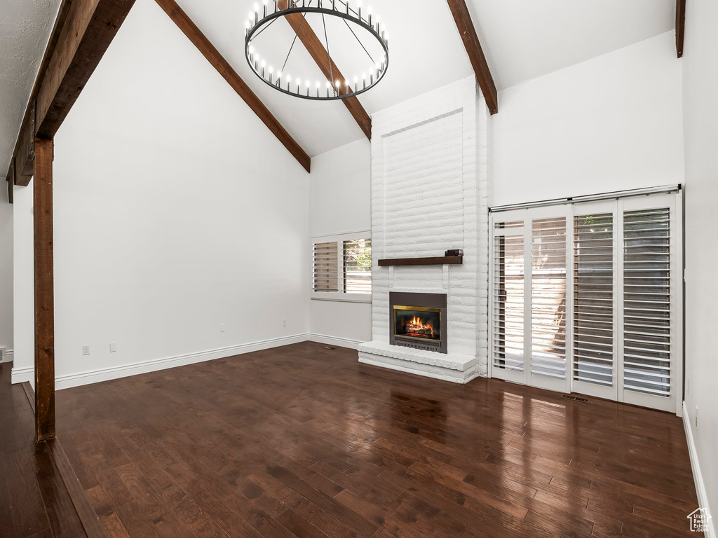 Unfurnished living room featuring beamed ceiling, high vaulted ceiling, a fireplace, a chandelier, and wood finished floors