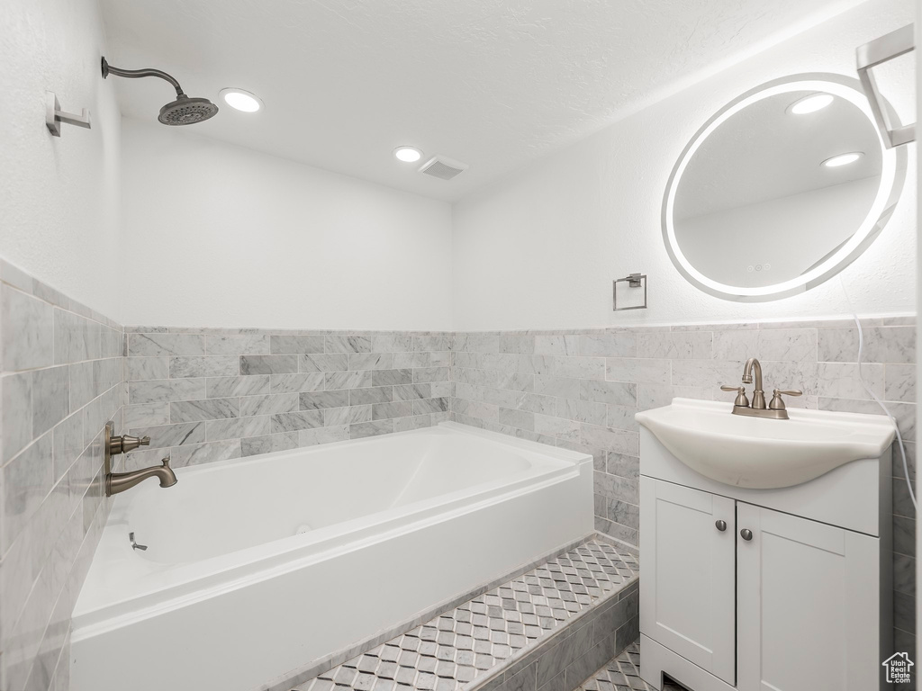 Full bath featuring a bath, vanity, recessed lighting, tile walls, and wainscoting