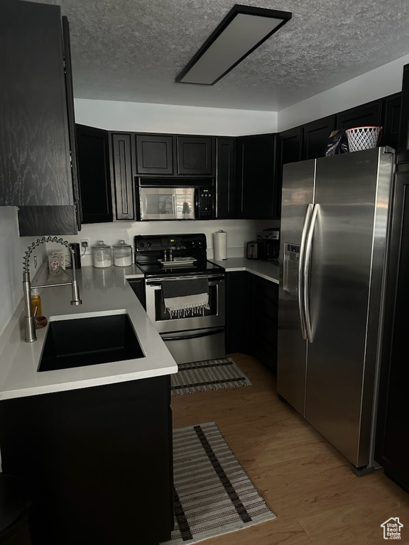 Kitchen featuring stainless steel appliances, dark cabinetry, a textured ceiling, light countertops, and light wood-style floors