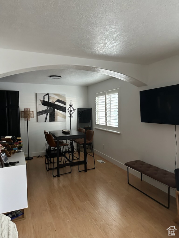 Dining room featuring a textured ceiling, light wood-style flooring, and arched walkways