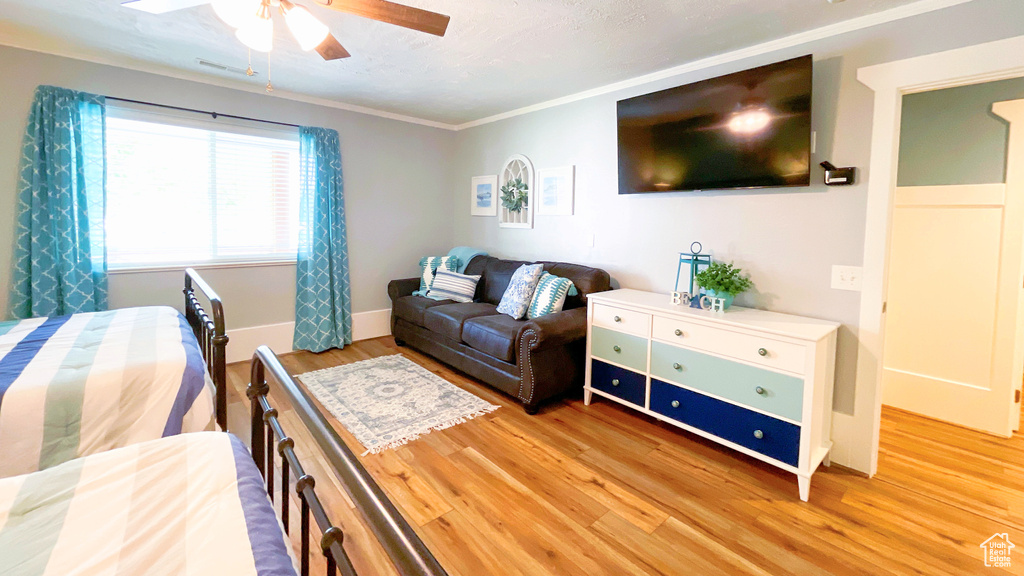 Bedroom with light wood finished floors, ornamental molding, and a ceiling fan