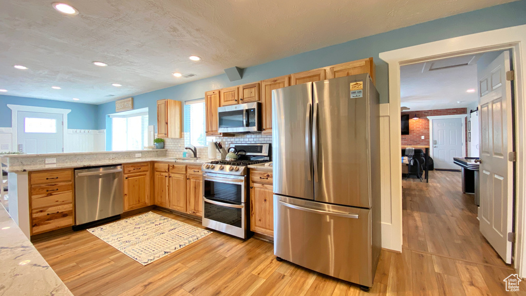 Kitchen with stainless steel appliances, light wood-type flooring, light brown cabinetry, tasteful backsplash, and a peninsula