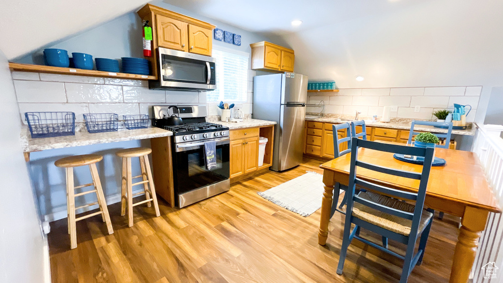 Kitchen featuring appliances with stainless steel finishes, decorative backsplash, open shelves, light wood-style floors, and vaulted ceiling