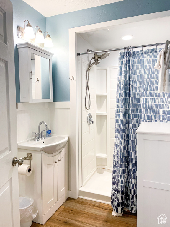 Full bath with wood finished floors, a shower stall, vanity, and a wainscoted wall