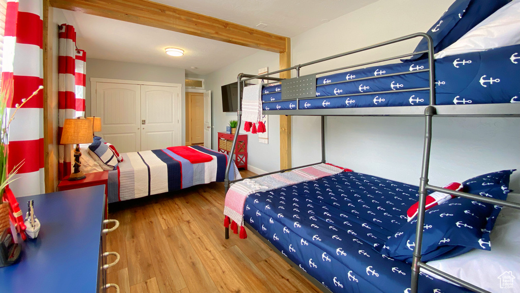Bedroom featuring wood finished floors, beamed ceiling, and a closet