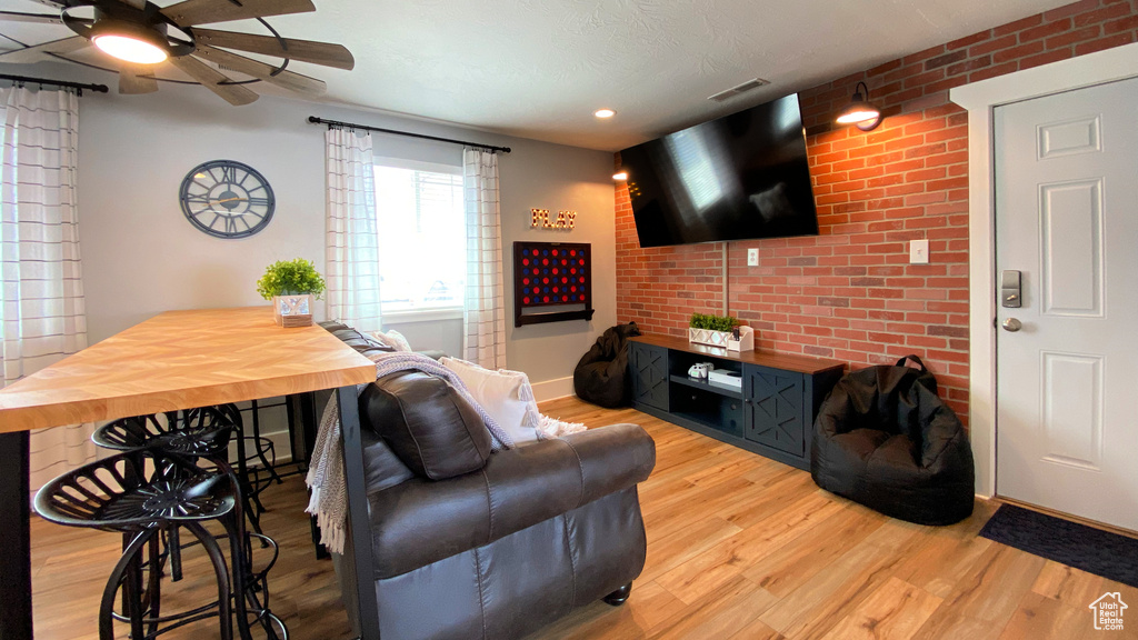 Living room with a ceiling fan, wood finished floors, brick wall, and recessed lighting