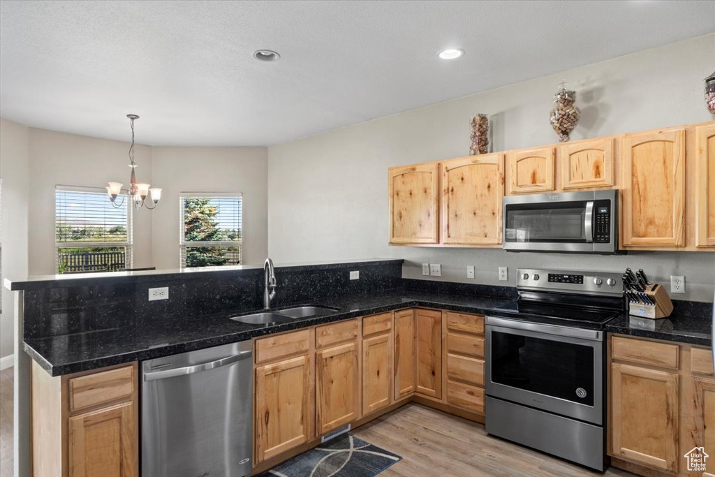 Kitchen with stainless steel appliances, a peninsula, a chandelier, light wood finished floors, and light brown cabinetry