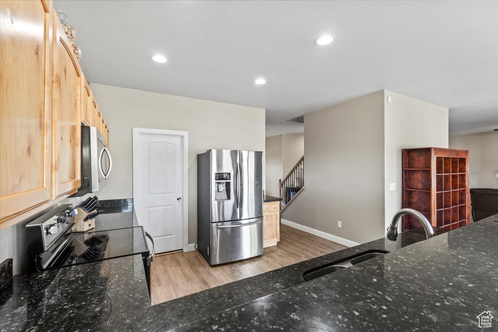Kitchen featuring stainless steel appliances, dark stone counters, light wood finished floors, recessed lighting, and light brown cabinetry