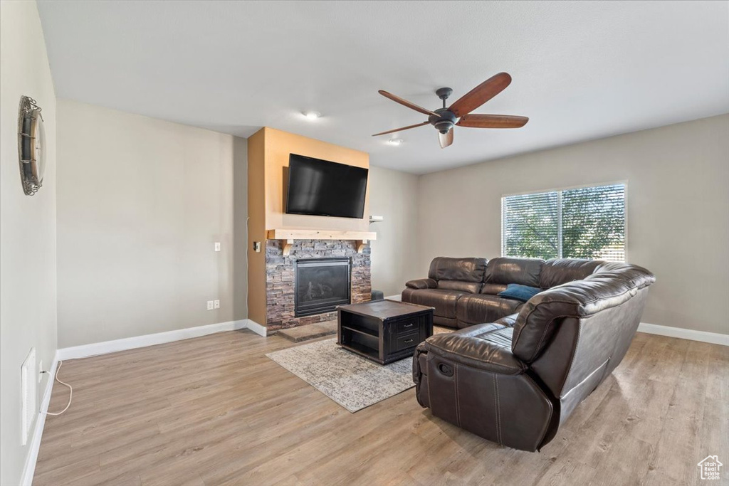 Living area featuring ceiling fan, light wood finished floors, and a stone fireplace