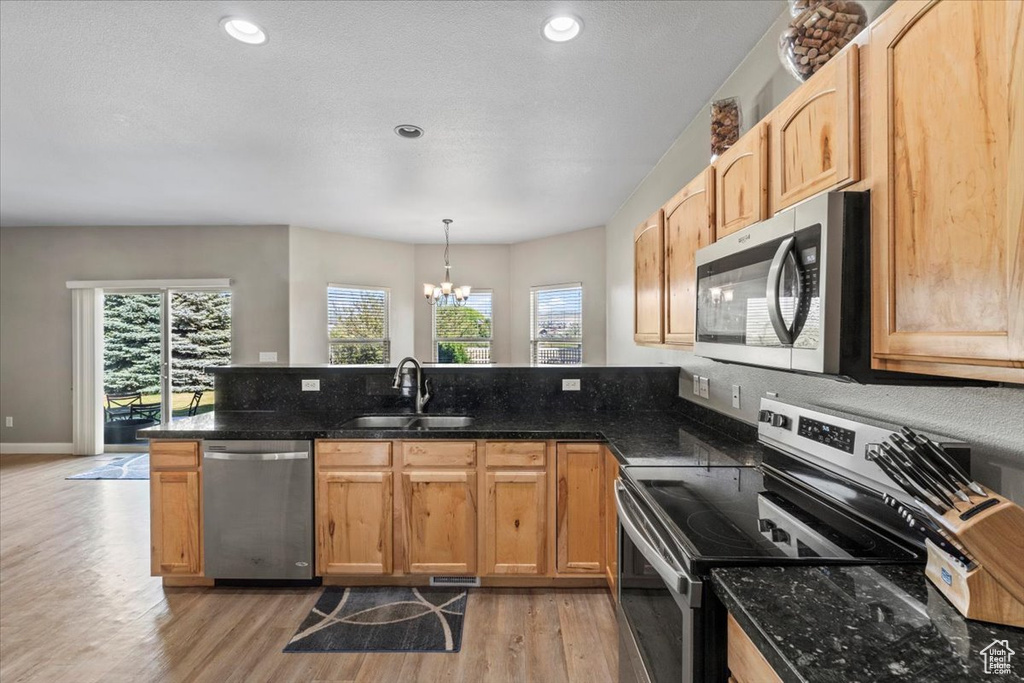 Kitchen with stainless steel appliances, light wood-type flooring, a chandelier, a peninsula, and dark stone counters