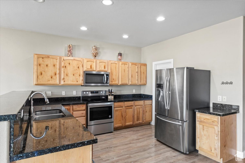 Kitchen featuring stainless steel appliances, light brown cabinetry, light wood-style floors, recessed lighting, and dark stone counters