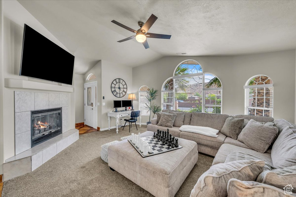 Carpeted living area with ceiling fan, vaulted ceiling, a tiled fireplace, and a desk