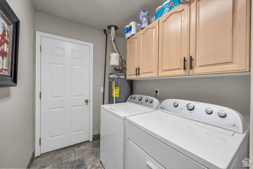 Washroom with water heater, washing machine and dryer, cabinet space, and stone finish flooring
