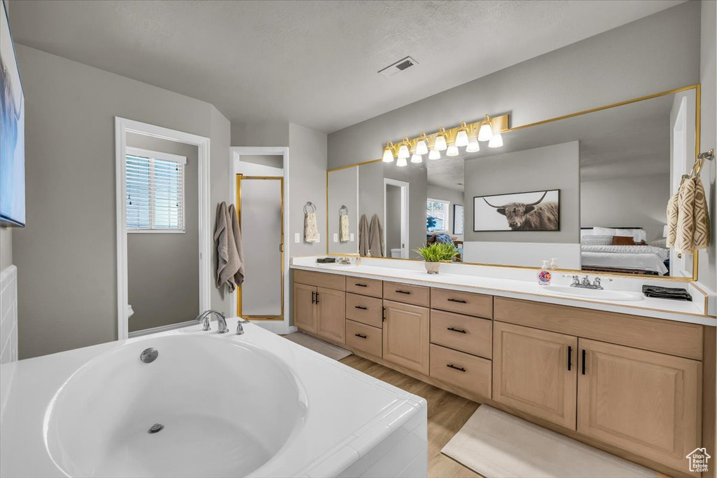 Ensuite bathroom featuring double vanity, healthy amount of natural light, a garden tub, and wood finished floors