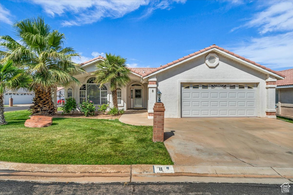 Mediterranean / spanish house featuring a tile roof, stucco siding, driveway, an attached garage, and a front yard