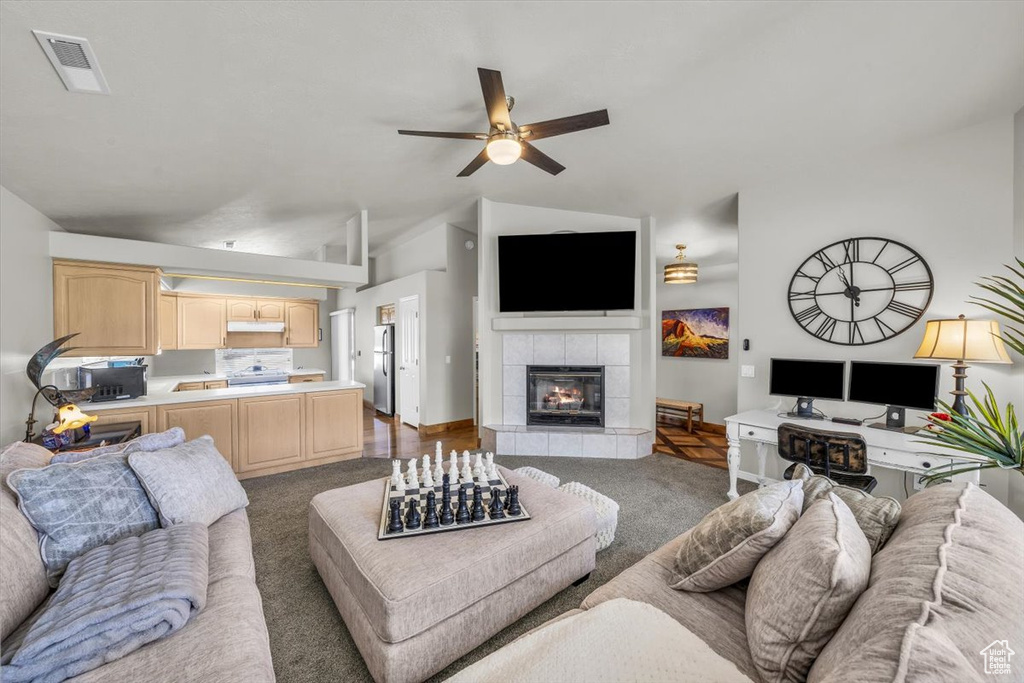 Living area featuring carpet flooring, a ceiling fan, a tiled fireplace, and lofted ceiling