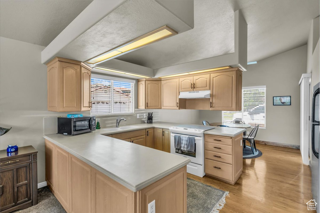 Kitchen with white range with electric stovetop, light brown cabinets, under cabinet range hood, and a peninsula