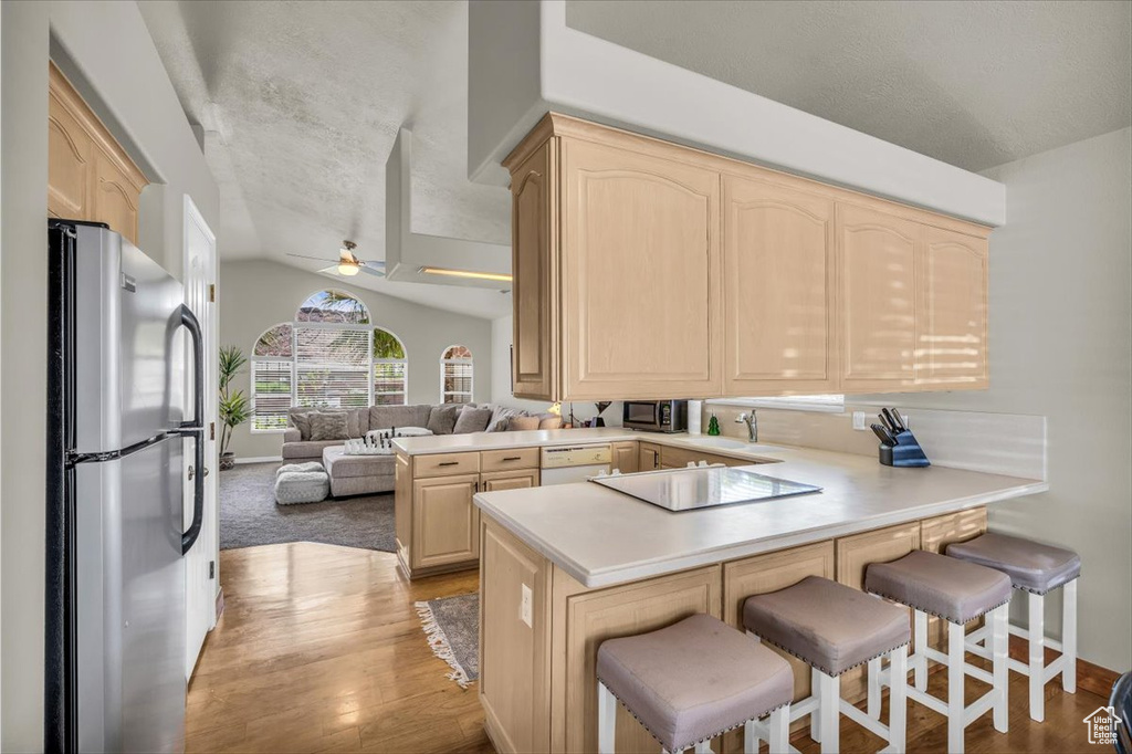 Kitchen featuring freestanding refrigerator, light brown cabinetry, a peninsula, electric cooktop, and light wood finished floors
