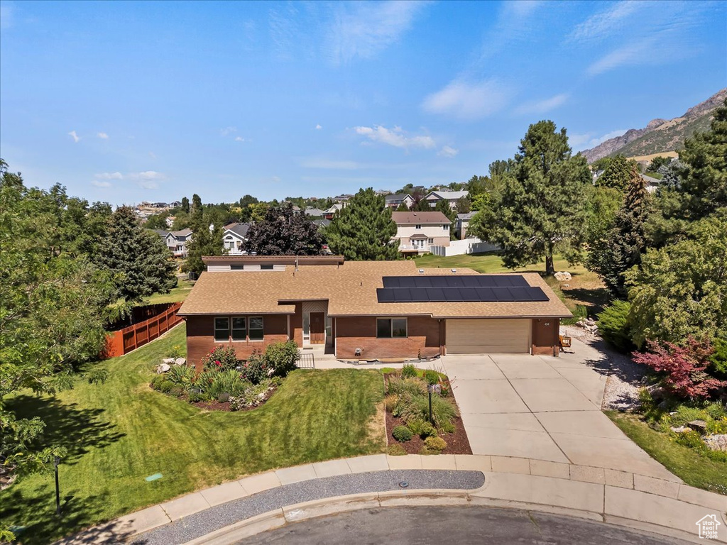 View of front facade featuring driveway, solar panels, an attached garage, and a shingled roof