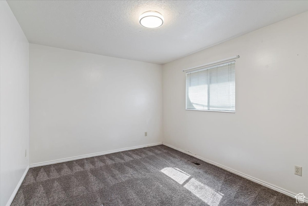 Unfurnished room featuring dark carpet and a textured ceiling