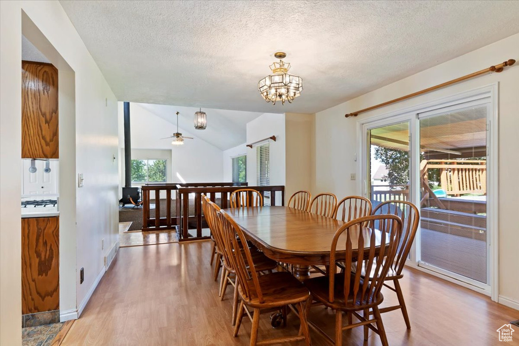 Dining space with light wood finished floors, a textured ceiling, a chandelier, ceiling fan, and lofted ceiling