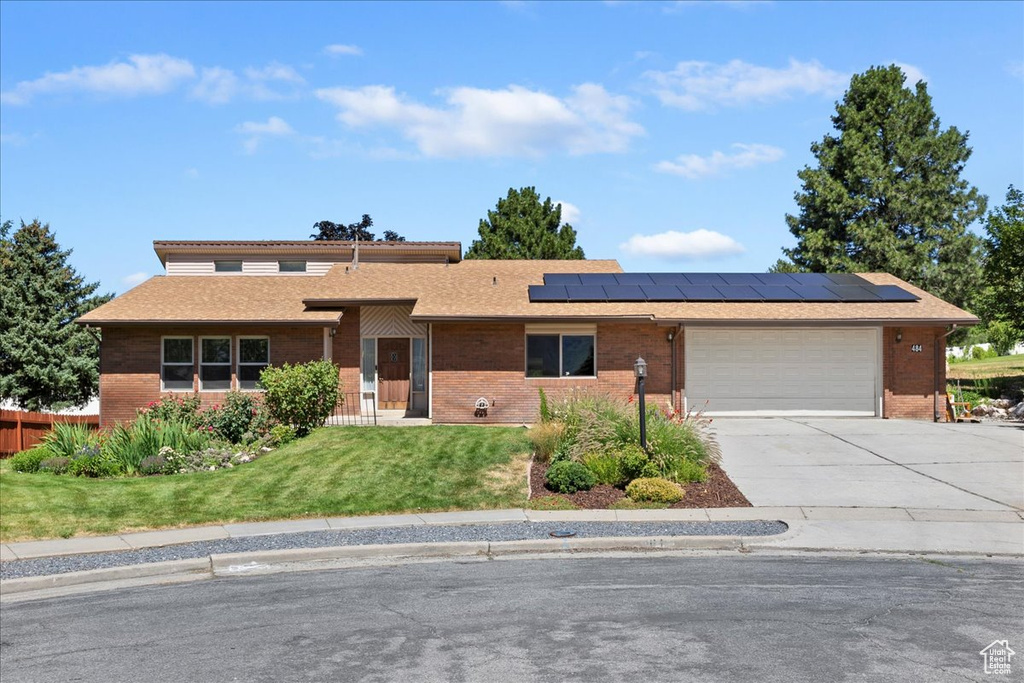 Single story home featuring driveway, brick siding, solar panels, and a garage