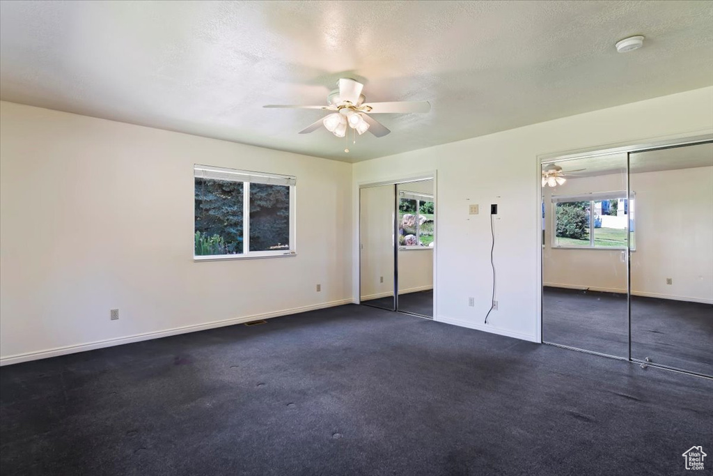 Unfurnished bedroom featuring multiple closets, multiple windows, dark colored carpet, and ceiling fan