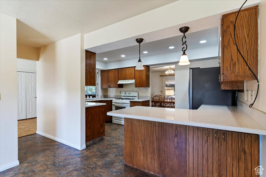 Kitchen with white gas range oven, freestanding refrigerator, a peninsula, light countertops, and recessed lighting