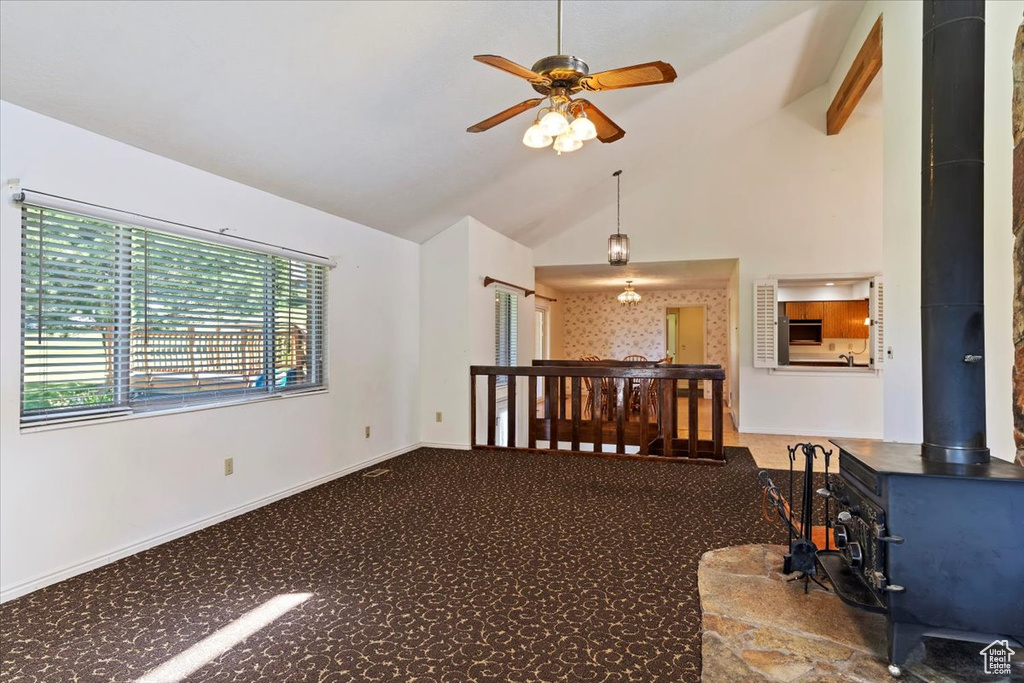 Carpeted empty room with a wood stove, ceiling fan, and high vaulted ceiling
