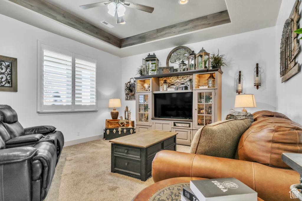 Living room featuring a ceiling fan, a tray ceiling, and light carpet