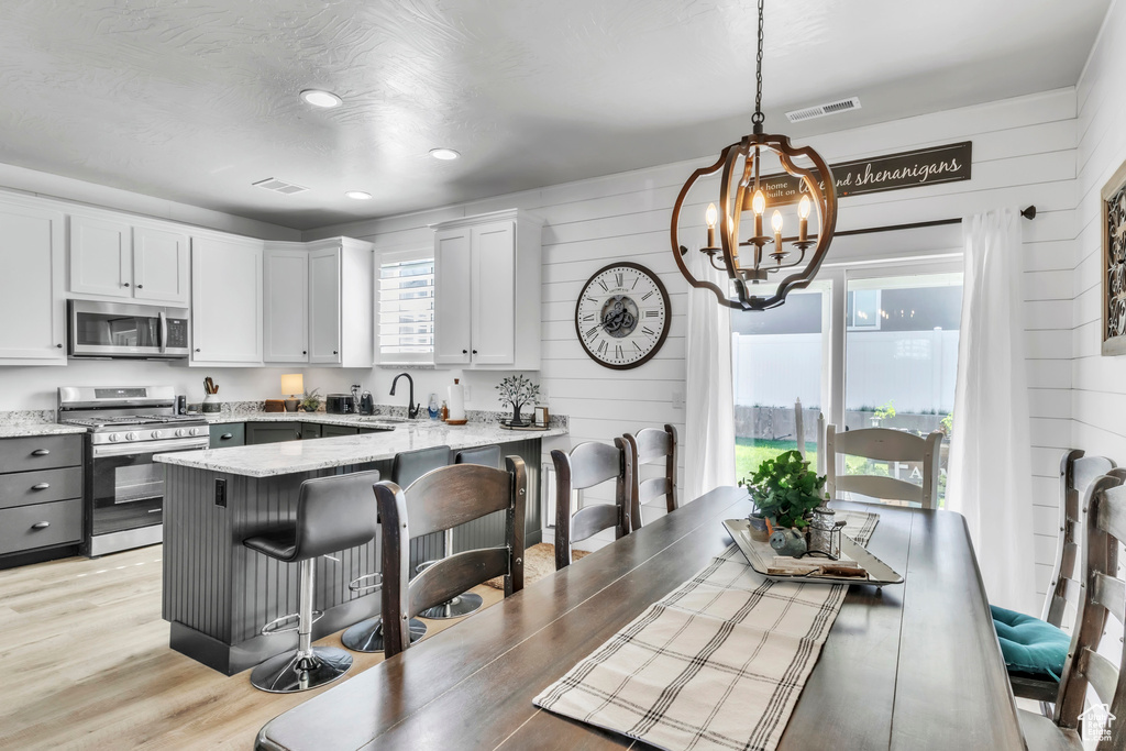 Kitchen with appliances with stainless steel finishes, a chandelier, wooden walls, light stone countertops, and a kitchen bar