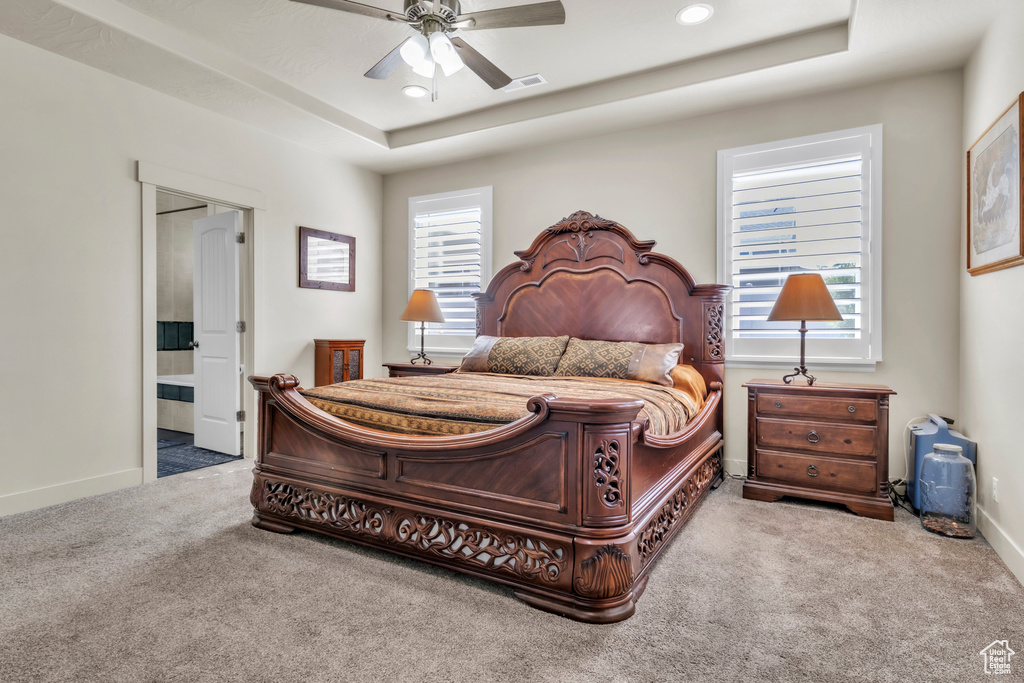 Carpeted bedroom with a tray ceiling, ensuite bath, recessed lighting, and a ceiling fan