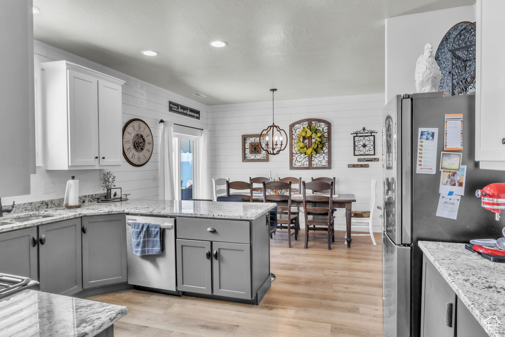 Kitchen featuring appliances with stainless steel finishes, a peninsula, light wood-style flooring, gray cabinets, and a chandelier