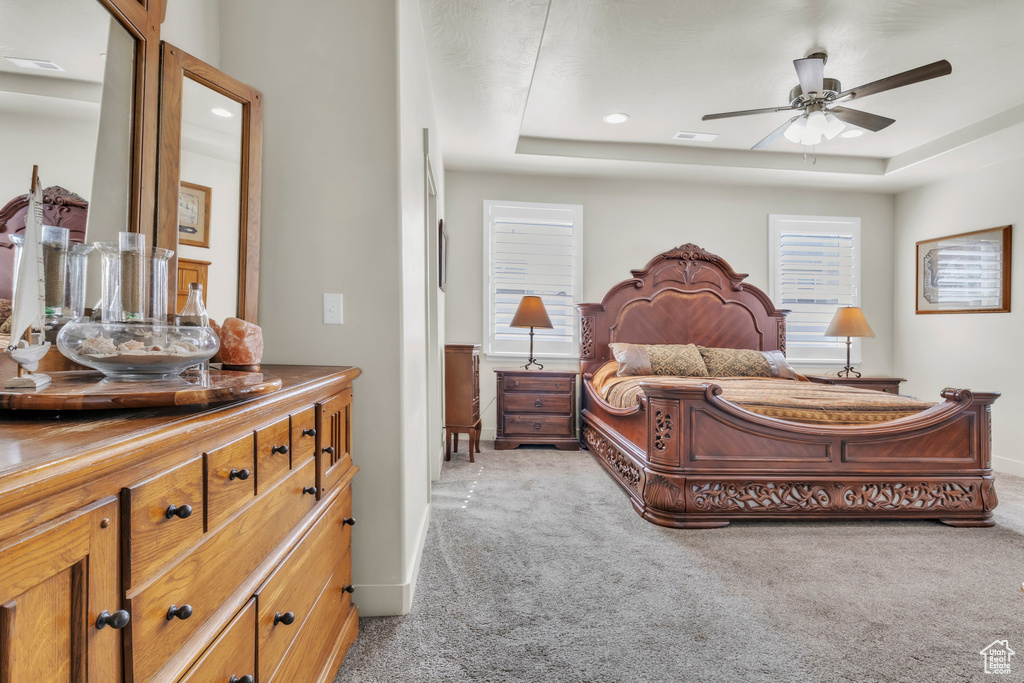 Bedroom with light colored carpet, a raised ceiling, and recessed lighting