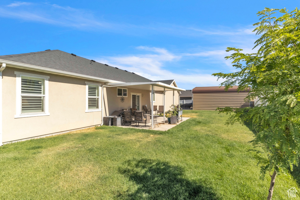 Rear view of property featuring a patio, a yard, stucco siding, and a shingled roof