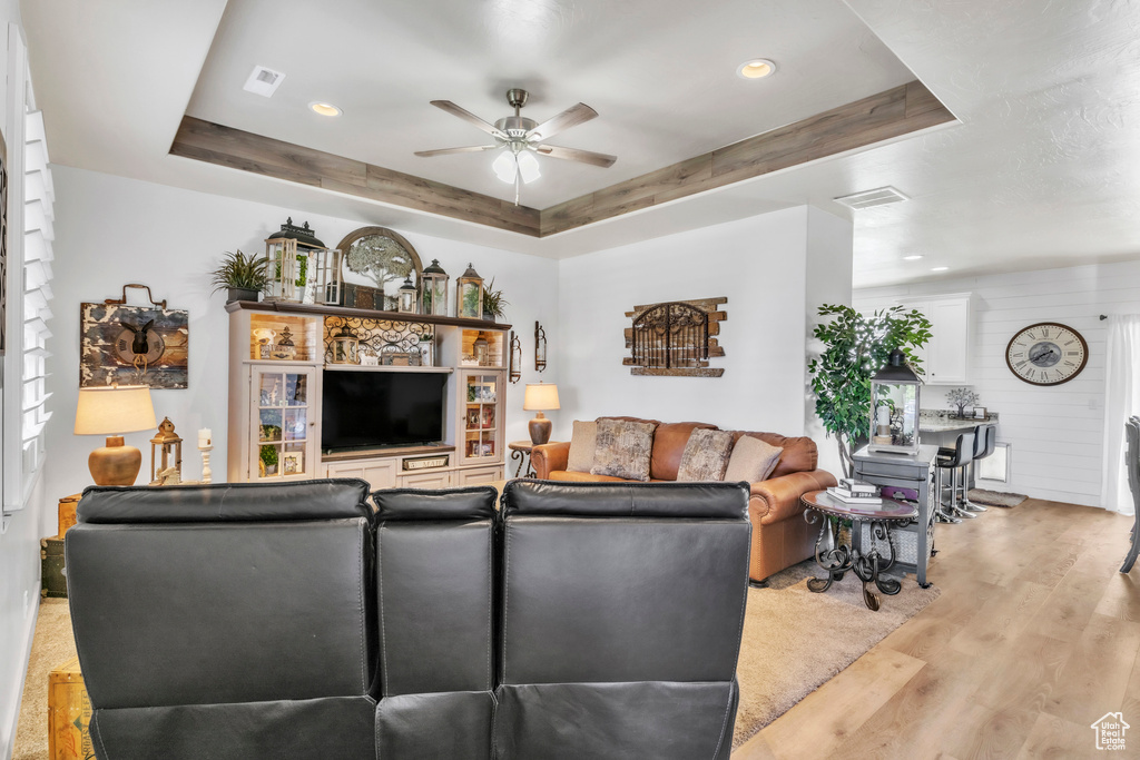 Living room featuring a ceiling fan, a raised ceiling, light wood finished floors, and recessed lighting