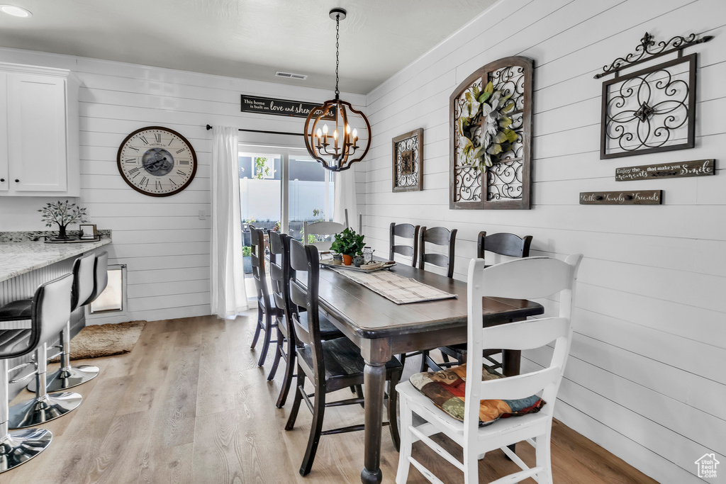 Dining room featuring wooden walls, light wood-style floors, and a chandelier