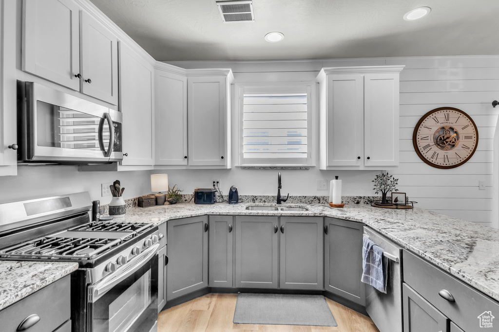 Kitchen featuring stainless steel appliances, gray cabinetry, light wood-type flooring, light stone counters, and white cabinetry