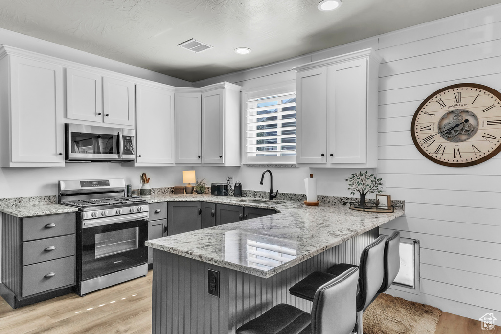 Kitchen featuring appliances with stainless steel finishes, a breakfast bar area, a peninsula, light stone counters, and wood walls