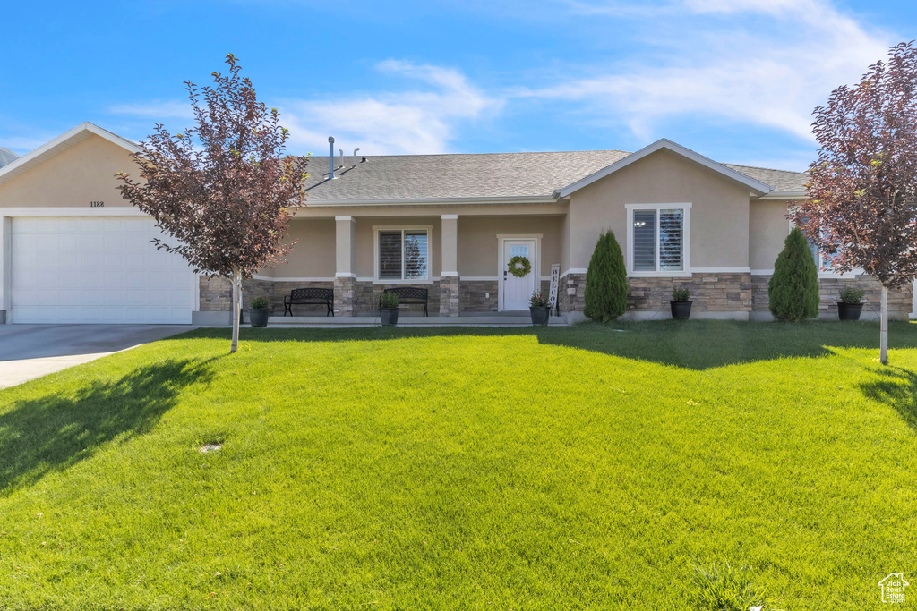 View of front of house with stucco siding, stone siding, a front lawn, and a garage