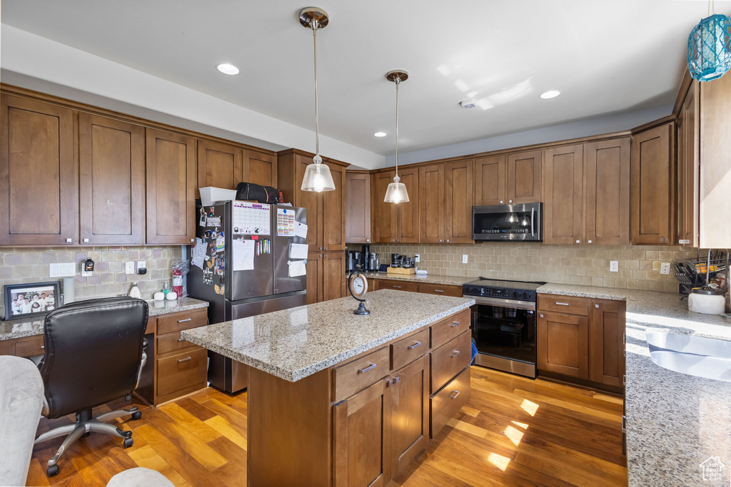 Kitchen with appliances with stainless steel finishes, light wood-style floors, tasteful backsplash, a center island, and decorative light fixtures