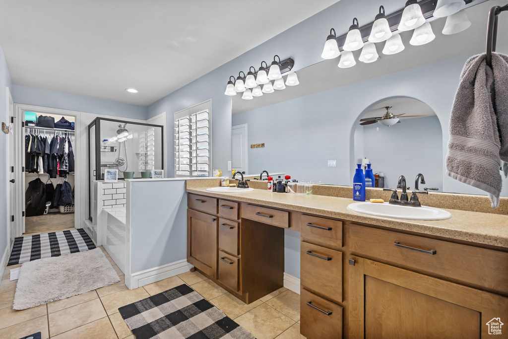 Bathroom featuring a shower stall, double vanity, tile patterned floors, a walk in closet, and a ceiling fan